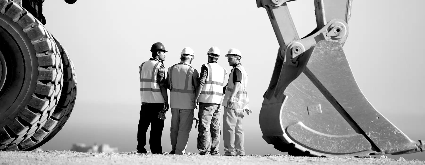 Cuatro trabajadores de la construcción hablando cerca de maquinaria pesada