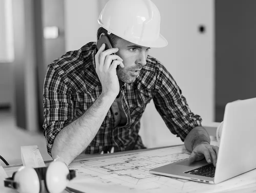 Trabajador de la construcción en la computadora y en el teléfono